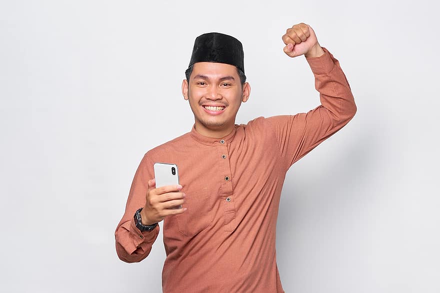 uomo musulmano, celebrazione, smartphone, vincitore, vittoria, eccitato, cellulare, successo, sorridente, gioia, positivo
