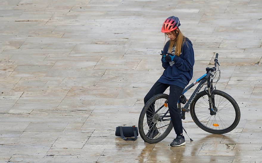menina, adolescente, capacete, bicicleta, pessoa, pavimento, assistindo, telefone, ouvindo, música