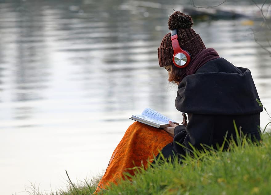 女性、聞いて、ヘッドホン、読む、本、草の上に座って、パーク、くつろぐ、湖、池、一人